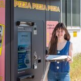 Reporterin Janka Hardenacke hält einen Pizza-Karton in der Hand und steht vor dem Pizza-Automaten an der Castroper Straße.