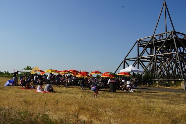 Bunte Sonnenschirme stehen neben Bierzeltgarnituren am Spurwerkturm auf der Halde Waltrop.