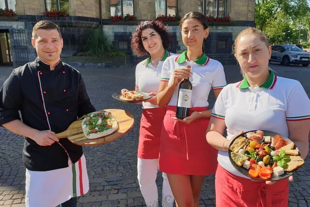 Das Team vom Ristaurante Stella steht auf dem Rathausplatz in Recklinghausen und hält Pizza, Pasta, Antipasti und Rotwein in die Kamera.
