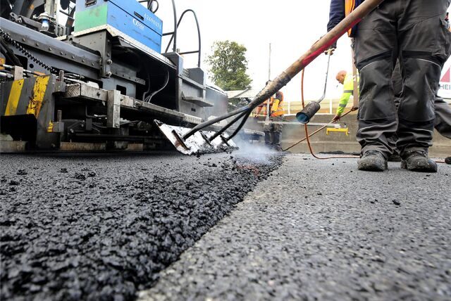 Arbeiter tragen auf einer Autobahn eine neue Asphaltdecke auf.