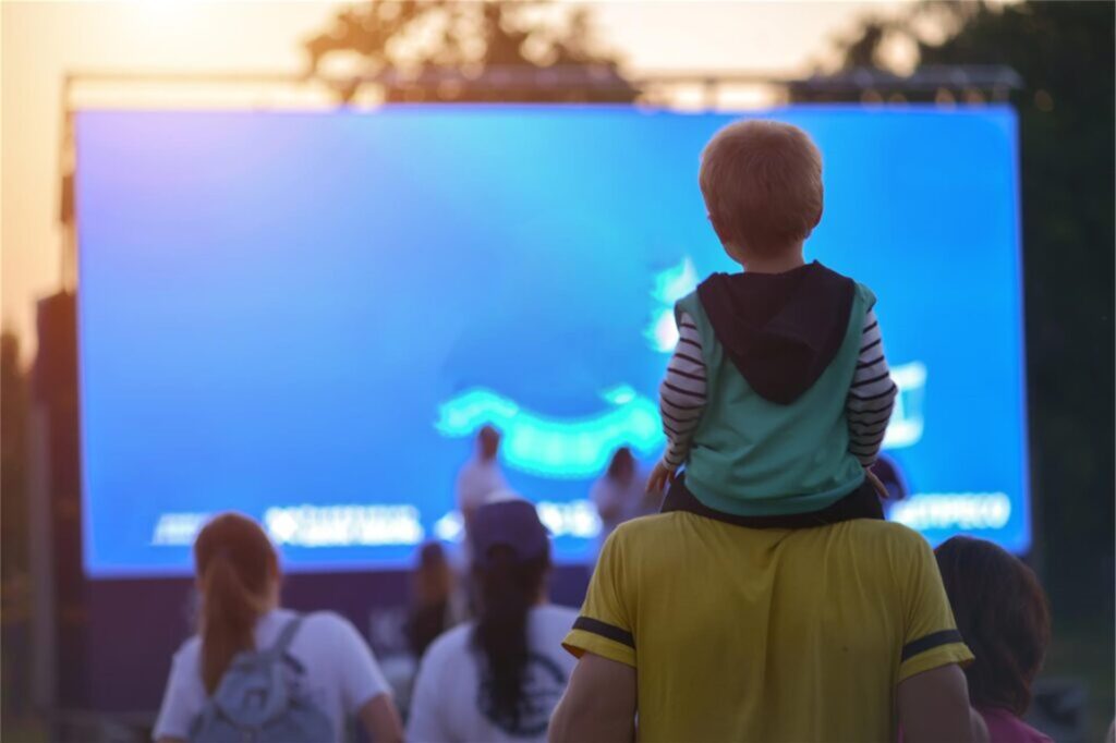 kind sitzt auf den schultern eines erwachsenen und guckt auf eine leinwand kind sitzt auf den schultern eines erwachsenen und guckt auf eine leinwand