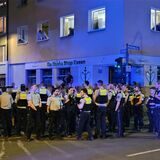 Polizisten stehen am Rande einer Massenschlägerei und riegeln eine Straße ab.