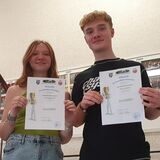 Ein Junge und ein Mädchen stehen im Flur einer Schule und halten Urkunden in den Händen.