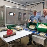 Zwei Männer präsentieren Spargel in grünen Boxen.