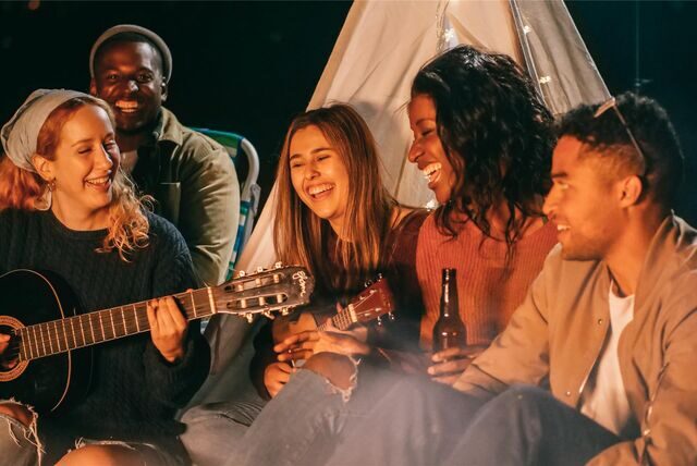 menschen sitzen am lagerfeuer, lachen und musizieren