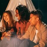 menschen sitzen am lagerfeuer, lachen und musizieren