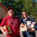 Ein Mann und eine Frau halten landwirtschaftliche Produkte in den Händen. Sie stehen vor einem Haus mit Ladenfront.