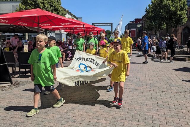 Kinder tragen die Fahne der Sportplatz-Olympiade und marschieren durch die Stadt.