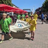 Kinder tragen die Fahne der Sportplatz-Olympiade und marschieren durch die Stadt.
