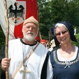 Ein Paar in mittelalterlichen Kostümen schaut lächelnd in die Kamera.