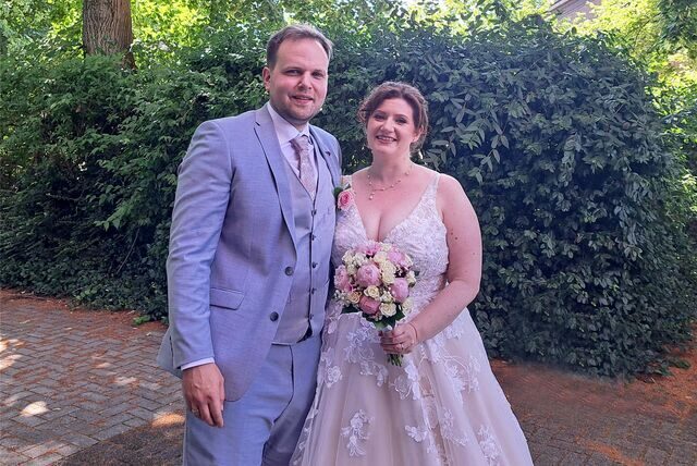 Das Brautpaar Jennifer und Iwan Iwancic hat sich in den Arm genommen und steht für ein Erinnerungsfoto vor eine Hecke.