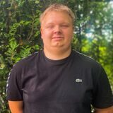 Florian Heickes steht vor einer grünen Hecke.