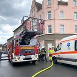Ein Drehleiterwagen der Feuerwehr und ein Krankentransporter stehen auf einer Straße.