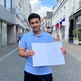 Der Recklinghäuser Abiturient Kusai Almousa hält sein Abi-Zeugnis in die Kamera und lächelt.