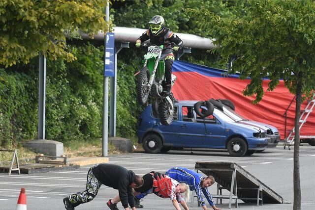 Ein Motorradfahrer springt über eine Rampe und drei am Boden liegende Menschen.