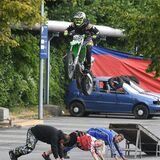 Ein Motorradfahrer springt über eine Rampe und drei am Boden liegende Menschen.