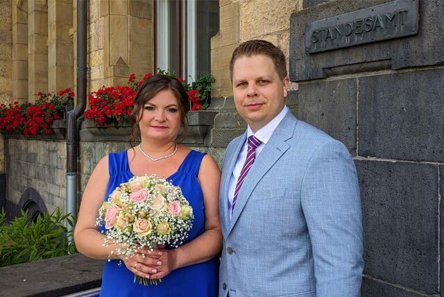 Zu sehen ist eine Braut in blauem Kleid und zu ihrer Rechten ihr Bräutigam in grauem Anzug.