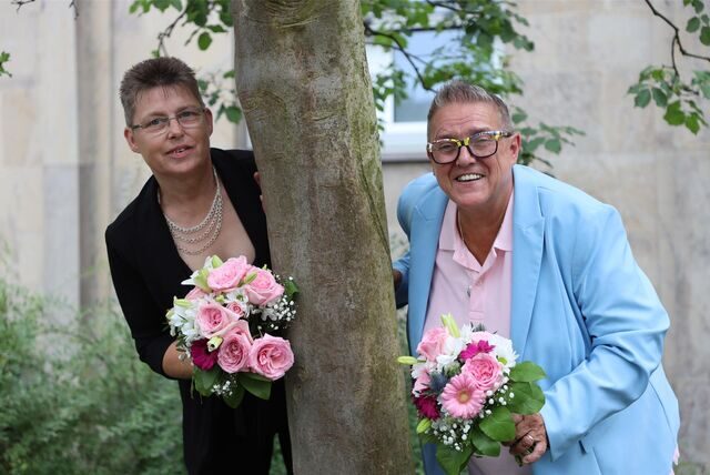 Hochzeitspaar Martina Knabke und Petra Burzynski aus Waltrop stehen links und rechts von einem Baum und halten Brautsträuße in den Händen.