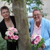 Hochzeitspaar Martina Knabke und Petra Burzynski aus Waltrop stehen links und rechts von einem Baum und halten Brautsträuße in den Händen.