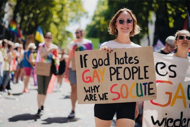 Eine Frau nimmt an einer Parade zum Christopher Street Day (CSD) in Köln teil – sie trägt ein Schild mit der Aufschrift „If god hates gay people, why are we so cute“.