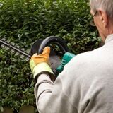 Ein Mann hält eine Kettensäge in der Hand und schneidet eine Hecke.