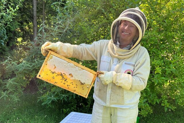 Regina Weyer in voller Imkerinnen-Montur mit Bienenwabe in der Hand.