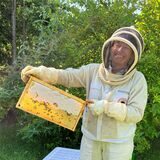 Regina Weyer in voller Imkerinnen-Montur mit Bienenwabe in der Hand.