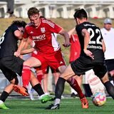 Zwei Spieler vom TuS Haltern im Dreikampf mit einem Spieler vom VfB Hüls; im Hintergrund sind Auswechselbank und Trainer des VfB Hüls unscharf sichtbar.