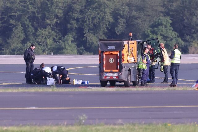 Sicherheitspersonal und Polizisten stehen auf dem Flugfeld und versuchen Aktivisten der Gruppe Letzte Generation vom Asphalt zu lösen, nachdem sie sich am 13. Juli festgeklebt haben.