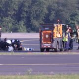 Sicherheitspersonal und Polizisten stehen auf dem Flugfeld und versuchen Aktivisten der Gruppe Letzte Generation vom Asphalt zu lösen, nachdem sie sich am 13. Juli festgeklebt haben.