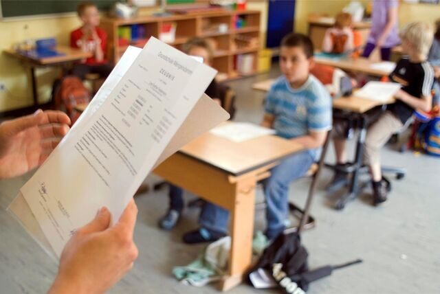 Ein Zeugnis ist im Vordergrund zu sehen, dahinter die Schüler einer Grundschul-Klasse