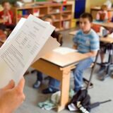 Ein Zeugnis ist im Vordergrund zu sehen, dahinter die Schüler einer Grundschul-Klasse