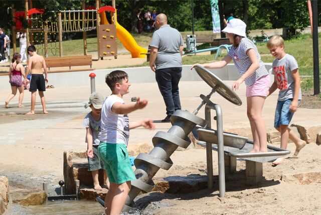 Bei Sommerwetter bieten Wasserspielplätze Familien Abkühlung und viel Spaß. Viele Kinder spielen in einem Becken mit Wasser in der Natur.