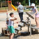 Bei Sommerwetter bieten Wasserspielplätze Familien Abkühlung und viel Spaß. Viele Kinder spielen in einem Becken mit Wasser in der Natur.