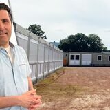 Ein Mann mit einem kurzärmligen Hemd. Im Hintergrund ist ein Containerdorf für Flüchtlinge zu sehen.