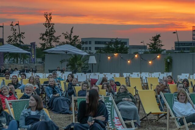 Menschen in Liegestühlen mit einem Sonnenuntergang im Hintergrund