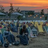 Menschen in Liegestühlen mit einem Sonnenuntergang im Hintergrund