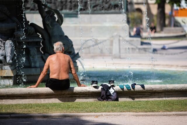 Ein Mann kühlt sich bei heißen Temperaturen an einem Brunnen in der Innenstadt ab.