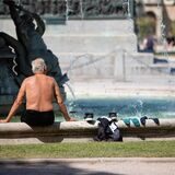 Ein Mann kühlt sich bei heißen Temperaturen an einem Brunnen in der Innenstadt ab.