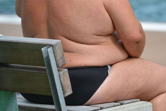 Ein übergewichtiger Mann sitzt in einem Freibad.