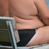 Ein übergewichtiger Mann sitzt in einem Freibad.