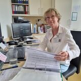 Eine Frau sitzt am Schreibtisch und blättert in Akten.