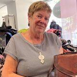 Heike Neumann hält in ihrem Laden der Castroper Altstadt eine braune Ledertasche in die Kamera. Im Hintergrund sieht man eine Vitrine mit Schmuck und voll bepackte Kleiderständer.