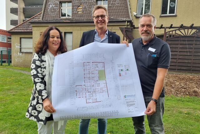 Drei Personen halten einen Bauplan hoch.
