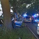 Polizei-Transporter vor Straßenbaum, mehrere Fahrzeuge mit Blaulicht drumherum