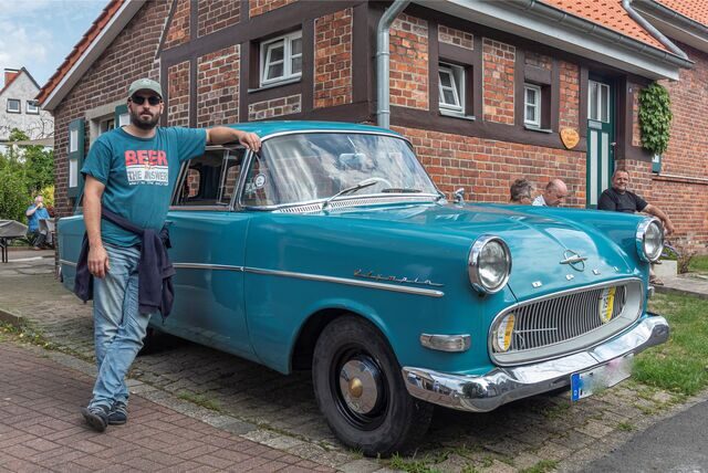Ein Mann steht neben einem alten Auto.