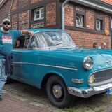 Ein Mann steht neben einem alten Auto.