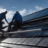 Arbeiter montieren eine PV-Anlage auf dem Dach eines Einfamilienhauses.
