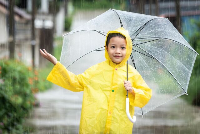 Asiatisches Kind hält einen Regenschirm und fängt Regenwasser mit der Hand.