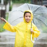 Asiatisches Kind hält einen Regenschirm und fängt Regenwasser mit der Hand.